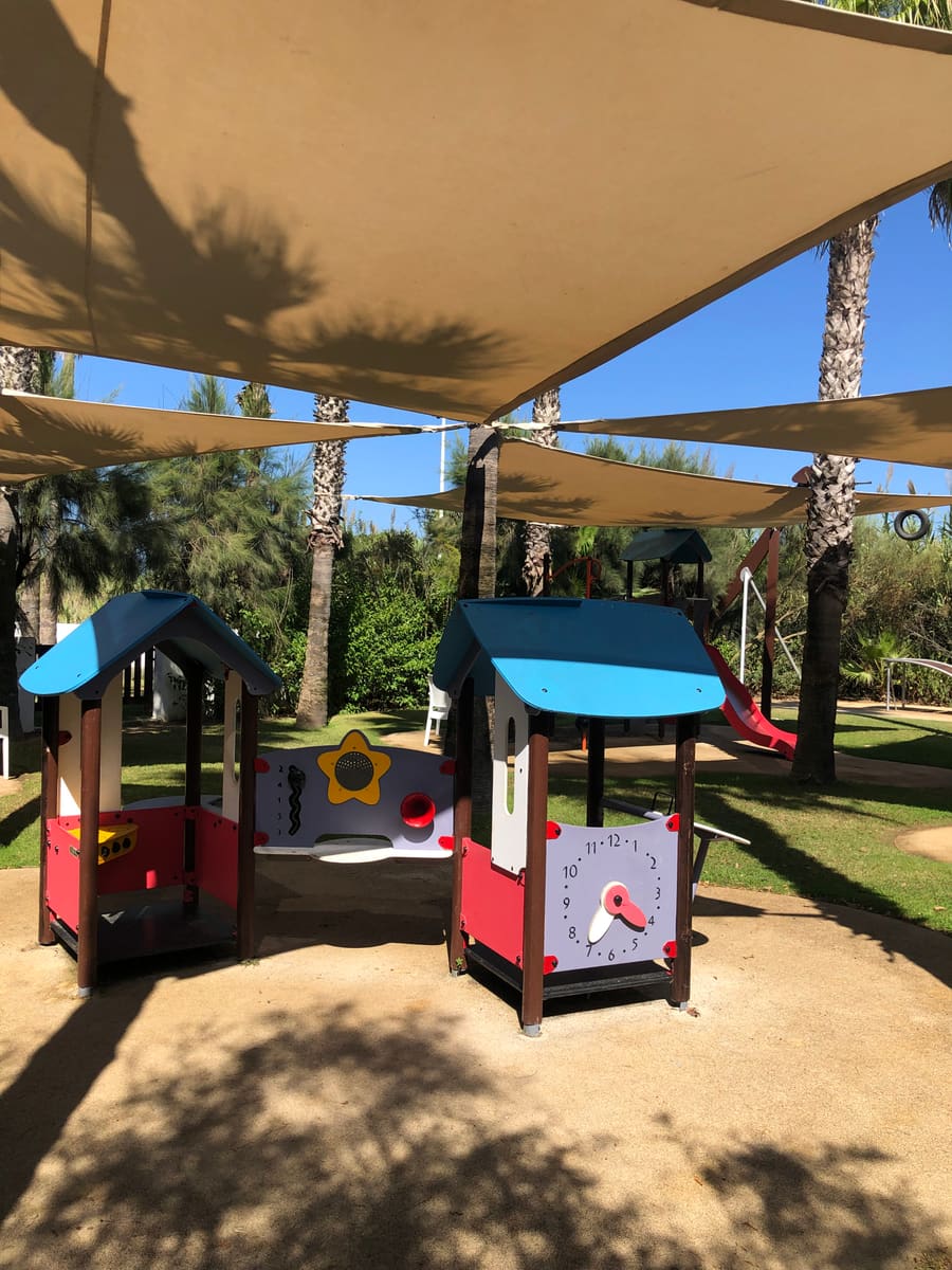 Parque infantil con casetas de juegos junto a las palmeras